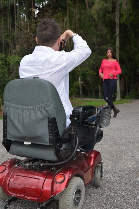 Berguim fotografando uma modelo de vestido vermelho em um parque, em sua cadeira de rodas motorizada.